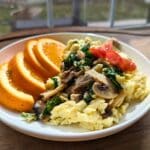 cottage cheese scrambled eggs with oranges on the side and veggies on top