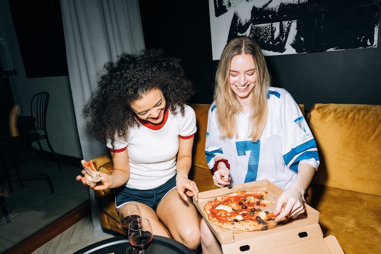 Two young women having fun and eating pizza on a cozy night in, capturing friendship and joy.
