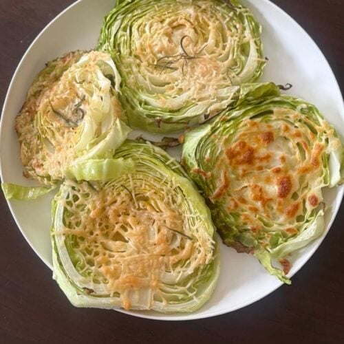 four cheesy cabbage steaks on a white plate