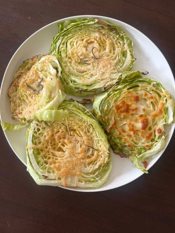 four cheesy cabbage steaks on a white plate