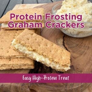 graham cracker sandwiches filled with protein frosting on a wood cutting board beside a small glass bowl of protein frosting