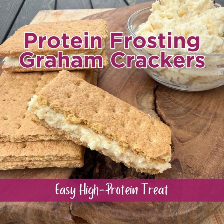 graham cracker sandwiches filled with protein frosting on a wood cutting board beside a small glass bowl of protein frosting