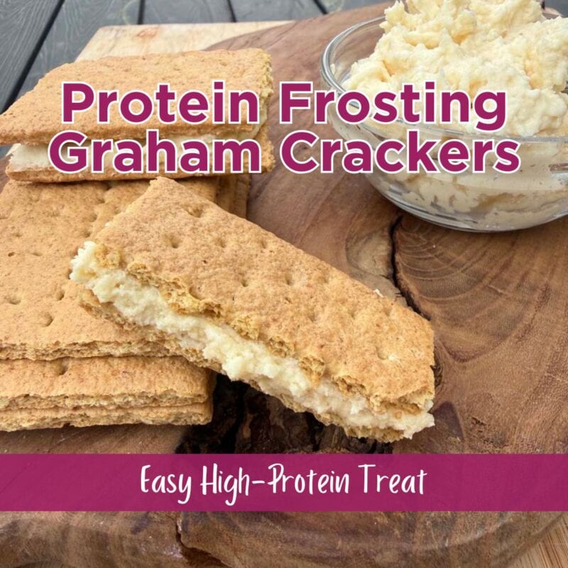 graham cracker sandwiches filled with protein frosting on a wood cutting board beside a small glass bowl of protein frosting