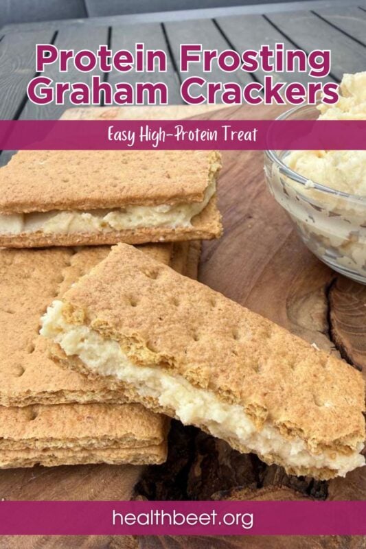 graham cracker sandwiches filled with protein frosting on a wood cutting board beside a small glass bowl of protein frosting