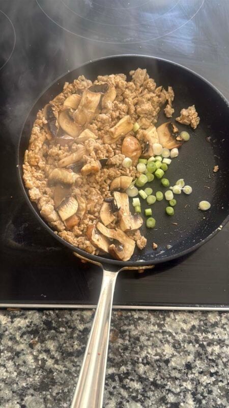 ground chicken, mushrooms, and green onions cooking in a pan on a stovetop