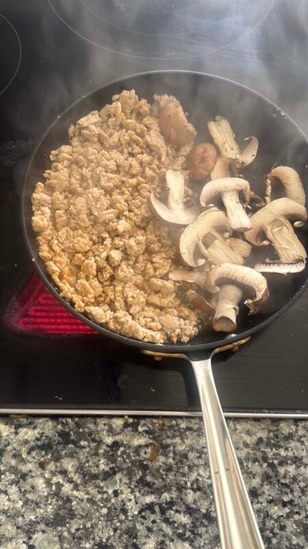 ground chicken and mushrooms cooking in a pan on a stovetop